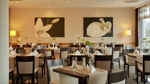 A restaurant with tables set for dining, featuring artwork on the walls. - Sunday Hotel Leipzig-Halle Standard Room (Landsberg-Peißen)