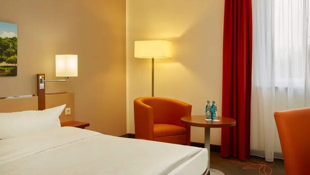 A hotel room with a bed, a desk, a chair, a lamp, and a window with curtains. - Sunday Hotel Leipzig-Halle Standard Room (Landsberg-Peißen)