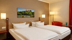 Una camera d'albergo con due letti, un quadro raffigurante un castello, due lampade da comodino, una sedia rossa e un tavolino con delle bottiglie.