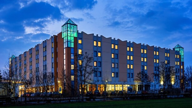 Un hotel moderno a più piani, caratterizzato da una torre in vetro ben visibile e una facciata luminosa.