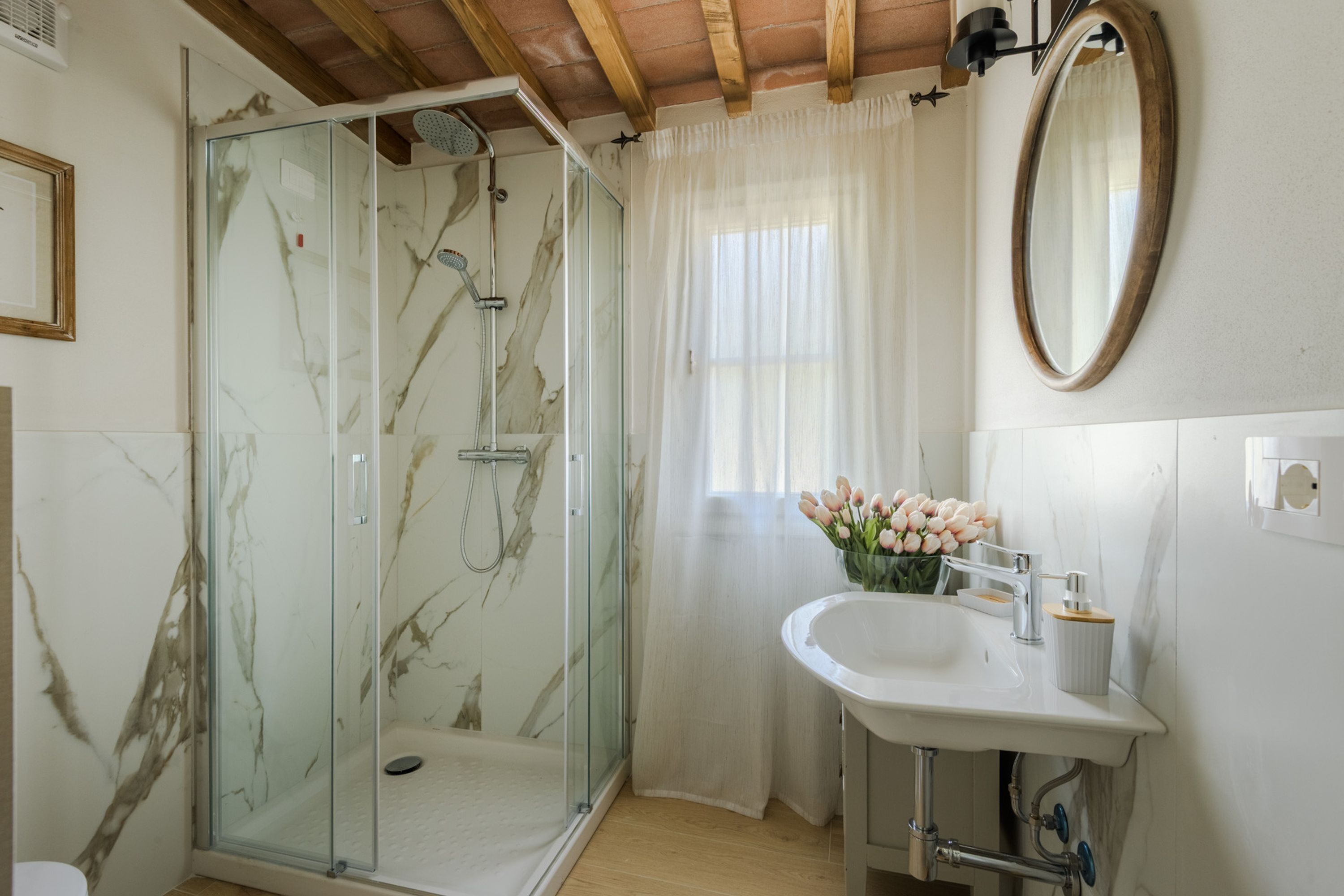 Un baño con cabina de ducha de vidrio, lavabo, espejo y ventana con cortina.