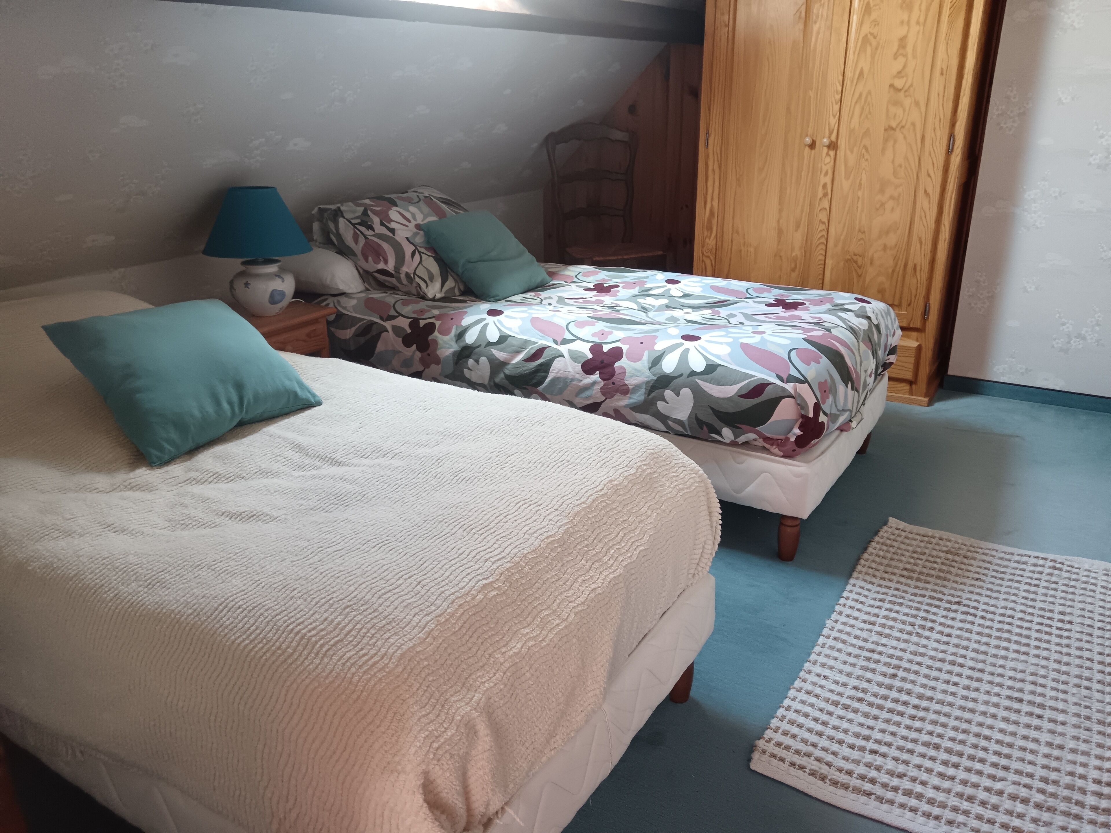 Une chambre avec deux lits, une armoire en bois, une table de chevet et un tapis à motifs.