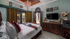 A bedroom with a large bed, a wooden dresser, a television, and a chandelier.