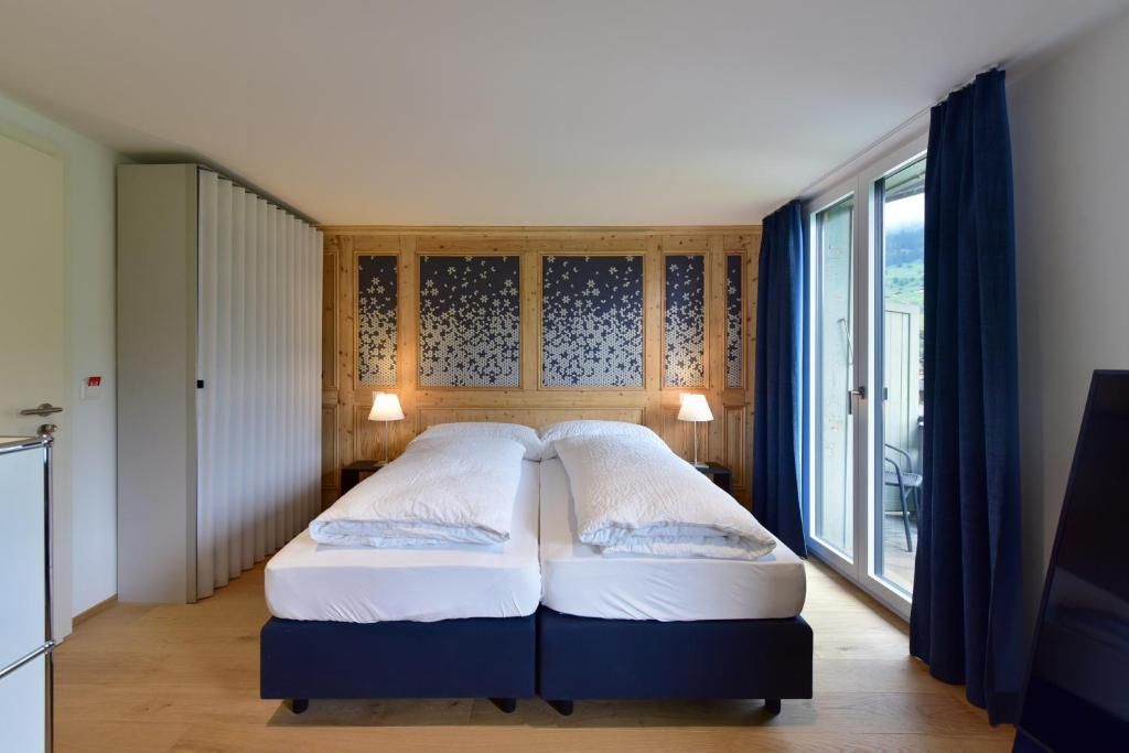Cama doble con dos almohadas, cabecero de madera y vistas al exterior a través de un ventanal grande.