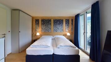 Cama doble con dos almohadas, cabecero de madera y vistas al exterior a través de un ventanal grande.