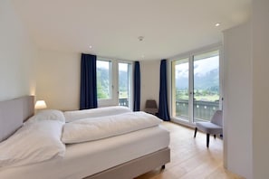 Une chambre d’hôtel avec un grand lit, deux fenêtres, une chaise et un balcon avec vue.