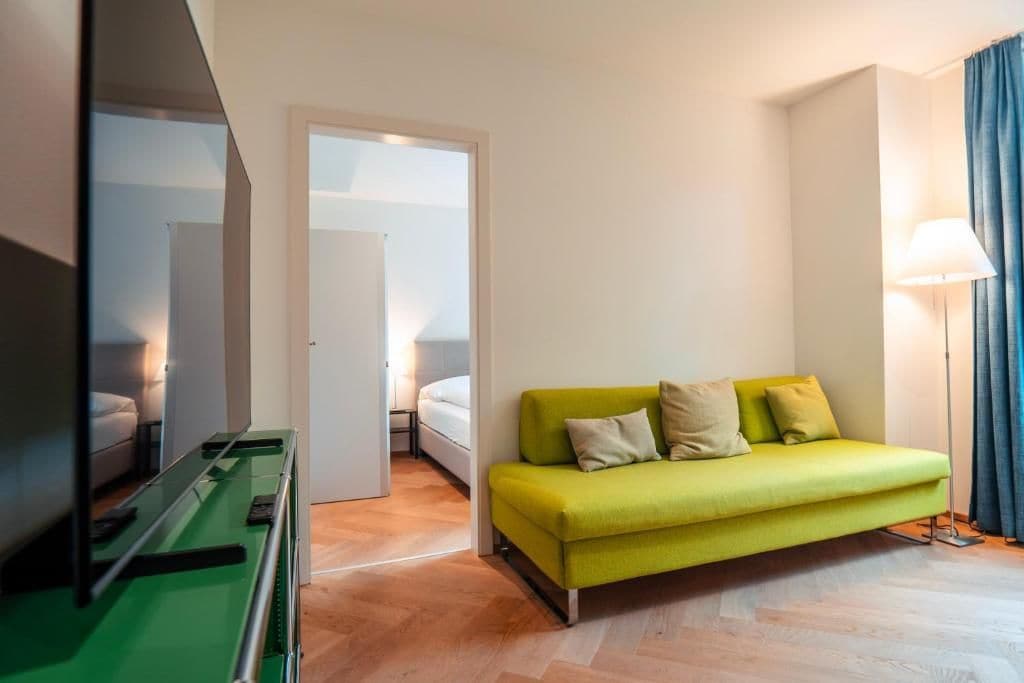 A room with a green sofa, a bed, a mirror, and a lamp.