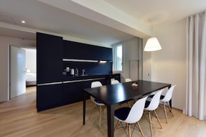 A modern kitchen with dark cabinetry, a dining table with white chairs, and a pendant light.