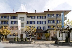 A multi-story hotel with a central entrance, balconies on each floor, and a flag on the right.