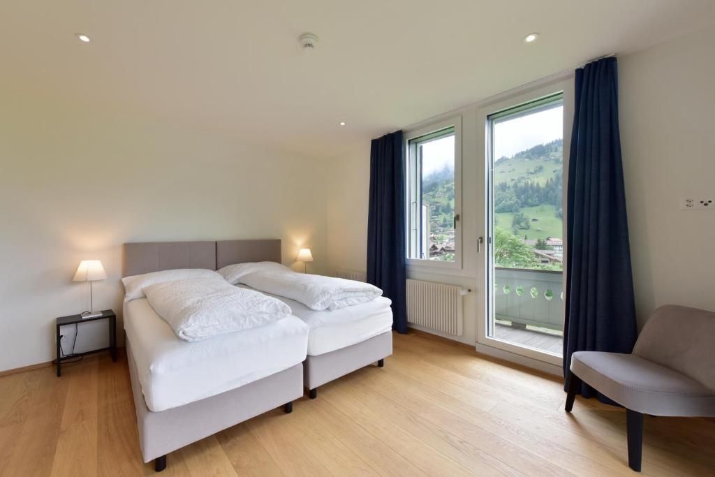 Ein Hotelzimmer mit Doppelbett, einem Nachttisch mit Lampe, einem Sessel und einem großen Fenster mit Blick auf eine grüne Landschaft.