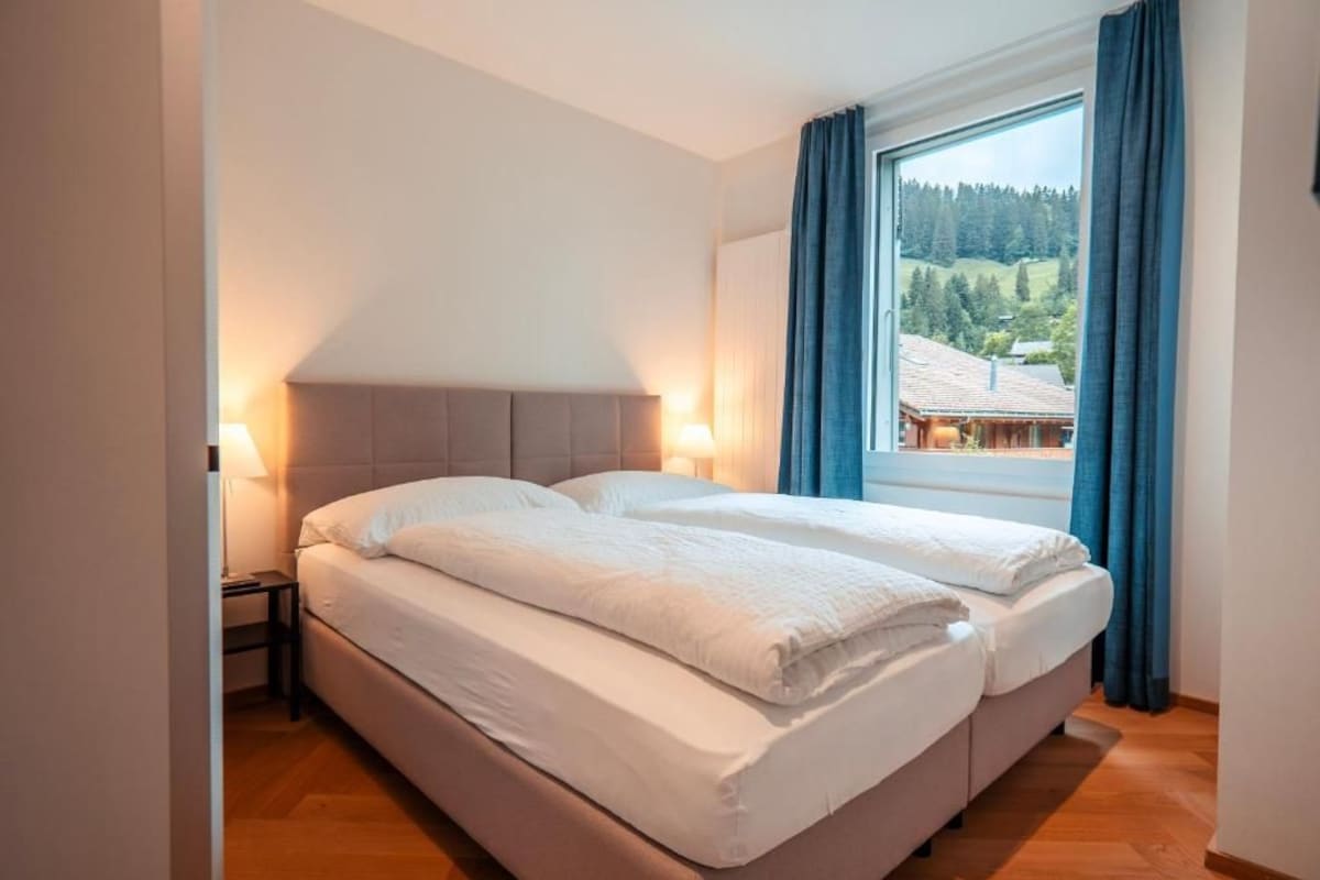 Une chambre avec deux lits, une fenêtre avec des rideaux et une vue sur une zone boisée.