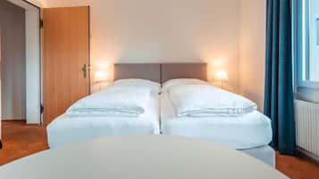 Ein Doppelzimmer mit zwei Betten, einer Holztür, einem fenster mit Vorhängen und einem runden Tisch im Vordergrund.