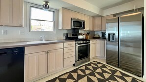 Una cocina moderna con armarios de tonos claros, electrodomésticos de acero inoxidable, microondas integrado y refrigerador.