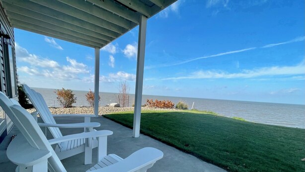 Un patio cubierto con sillas Adirondack blancas, piso de concreto y vista al agua.