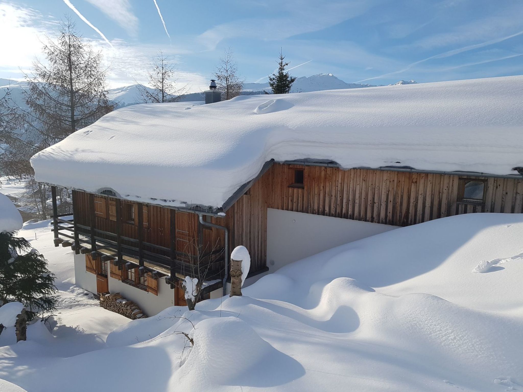 Une cabane en bois dont le toit est recouvert de neige, entourée d’un paysage enneigé et d’arbres couverts de neige.