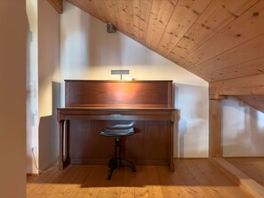 A room with a wooden desk and a chair, a slanted ceiling, and a light fixture on the wall.