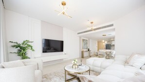 A modern living room with a flat-screen TV, white sofas, a round coffee table, and a potted plant. - Bloomfields 2BR plus Maid in Radiant  (Abu Dhabi)