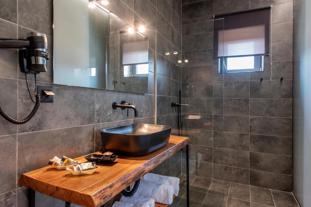 A modern bathroom with a large vessel sink, a wooden vanity, a hairdryer, and a mirror.