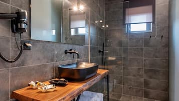 A modern bathroom with a large vessel sink, a wooden vanity, a hairdryer, and a mirror.