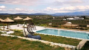 A pool with a hanging chair and umbrellas, surrounded by a stone wall and a view of distant mountains. - ALAGNI CRETAN RESORT (Alagni)
