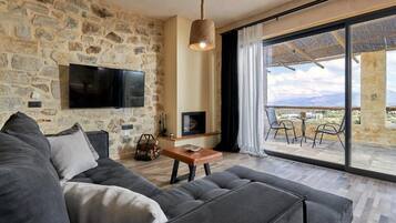 Una sala de estar con pared de piedra, televisor de pantalla plana, chimenea y un balcón con vistas.
