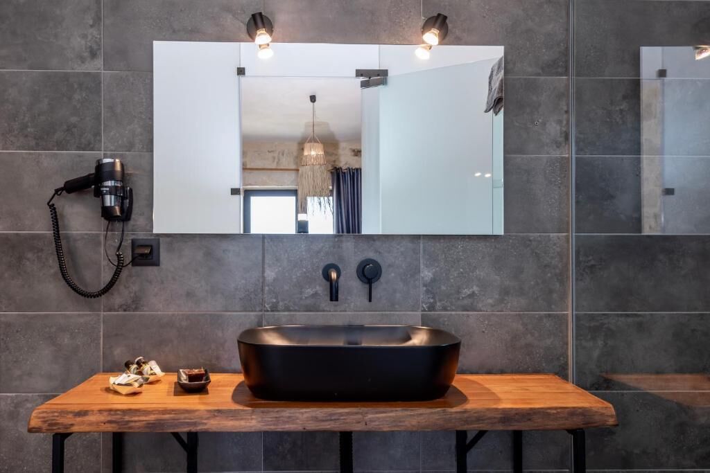 A modern bathroom with a large mirror, a black sink, and a hairdryer on the wall.