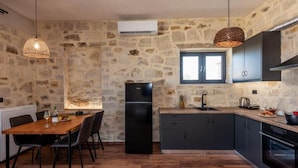 A kitchen with stone walls, a black refrigerator, a wooden dining table with chairs, and a window above the sink. - ALAGNI CRETAN RESORT (Alagni)