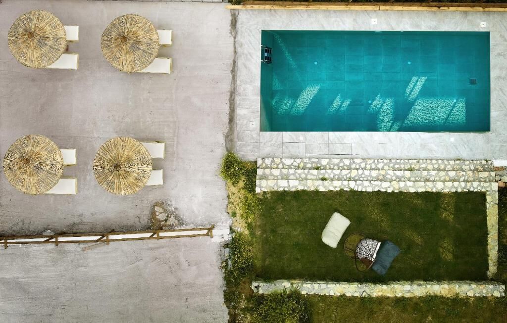 Vista aérea de una piscina con borde de piedra, rodeada de césped, una silla de descanso y una pequeña mesa.