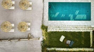 Vista aérea de una piscina con borde de piedra, rodeada de césped, una silla de descanso y una pequeña mesa.