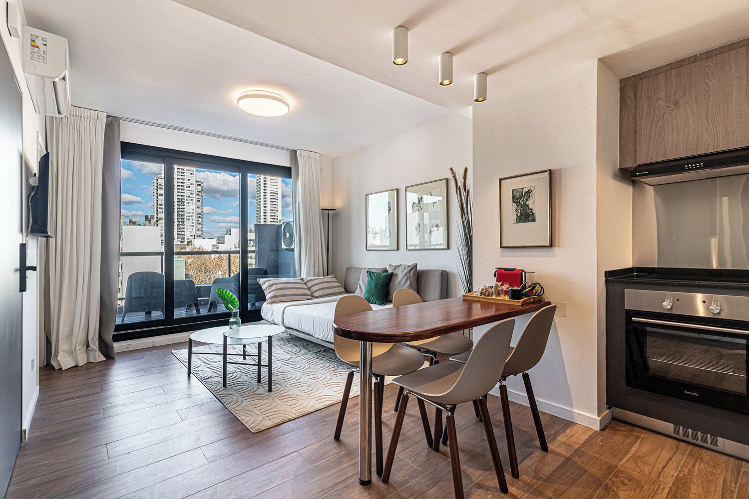 A modern apartment with a dining area, a sofa, a kitchen with a stove, and large windows with a city view.