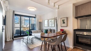 Ein modernes Apartment mit Essbereich, einer Couch, einer Küche mit Herd und großen Fenstern mit Stadtblick.
