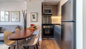 Eine kompakte Küche mit Mikrowelle, Backofen und Kühlschrank. Im angrenzenden Wohnbereich befindet sich ein Esstisch mit Stühlen sowie eine Couch.