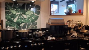 Ett kök med en spis, kastruller, en grill och ett fönster med utsikt över omgivningen.