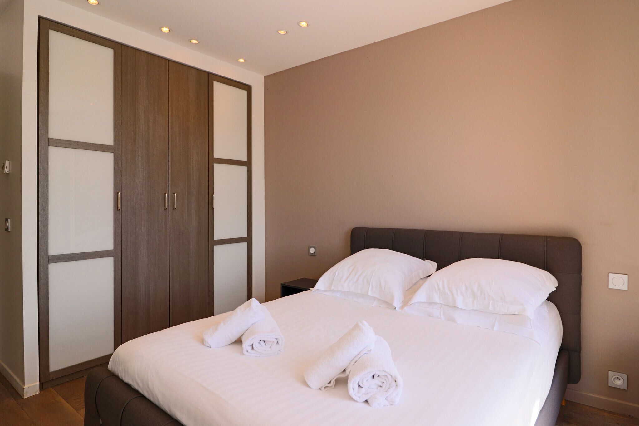 A hotel room with a large bed, two pillows, a nightstand, and a wardrobe with sliding doors.