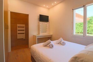 A hotel room with a bed, a vanity with a mirror and lights, a television, and a window with a view of greenery. - Modern Villa in a Quiet Location, 10' from the Center (Antibes)