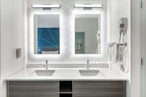 A bathroom with two sinks, a mirror, a hairdryer, and a towel rack. - City Express by Marriott Redmond Airport (REDMOND)