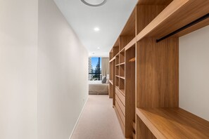 A hallway with a built-in wooden shelving unit, a bed with a view of trees, and a carpeted floor. - The Coastal Luxe Haven - Coolangatta (Gold Coast)