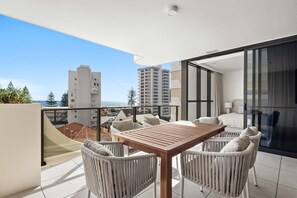 A balcony with a wooden table and wicker chairs, overlooking a cityscape and the sea. - The Coastal Luxe Haven - Coolangatta (Gold Coast)