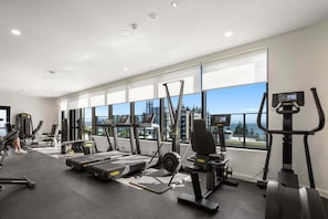Ein modernes Fitnessstudio mit Cardiogeräten, Gewichten und großen Fenstern mit Blick auf die Stadt.