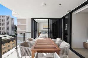 Een balkon met een houten tafel en witte rieten stoelen, met uitzicht op een stadsbeeld.