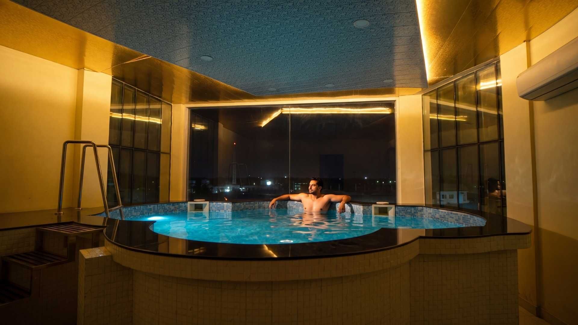 A man in a hot tub with a city view at night.
