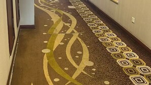 A hotel hallway with patterned carpet, doors, and a surveillance camera.