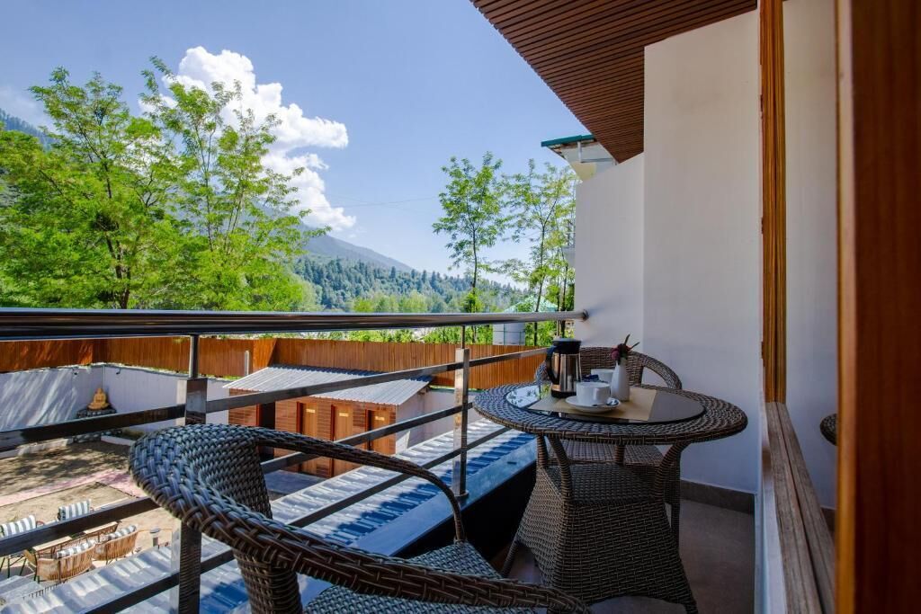 A balcony with wicker furniture, a table, and a view of trees and mountains.