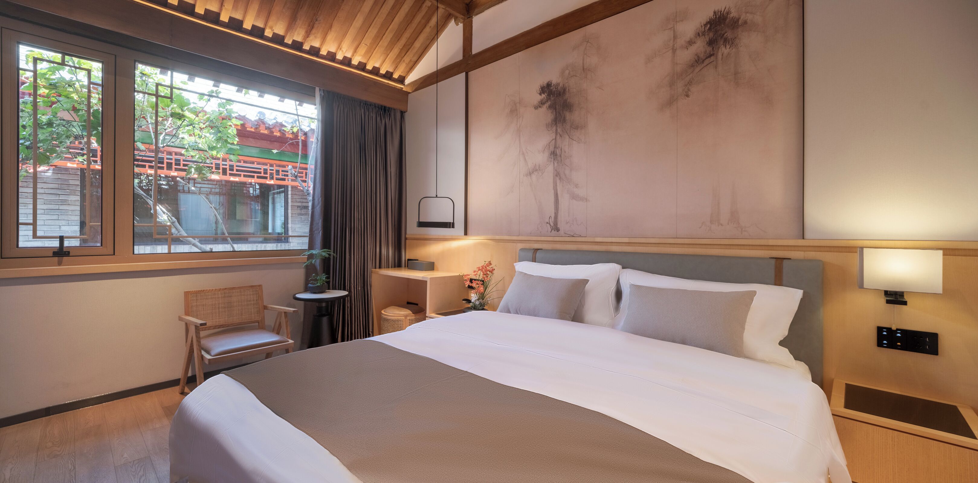 Une chambre d’hôtel avec un grand lit, un bureau, une chaise, une fenêtre donnant sur un immeuble et un mur orné d’œuvres d’art.