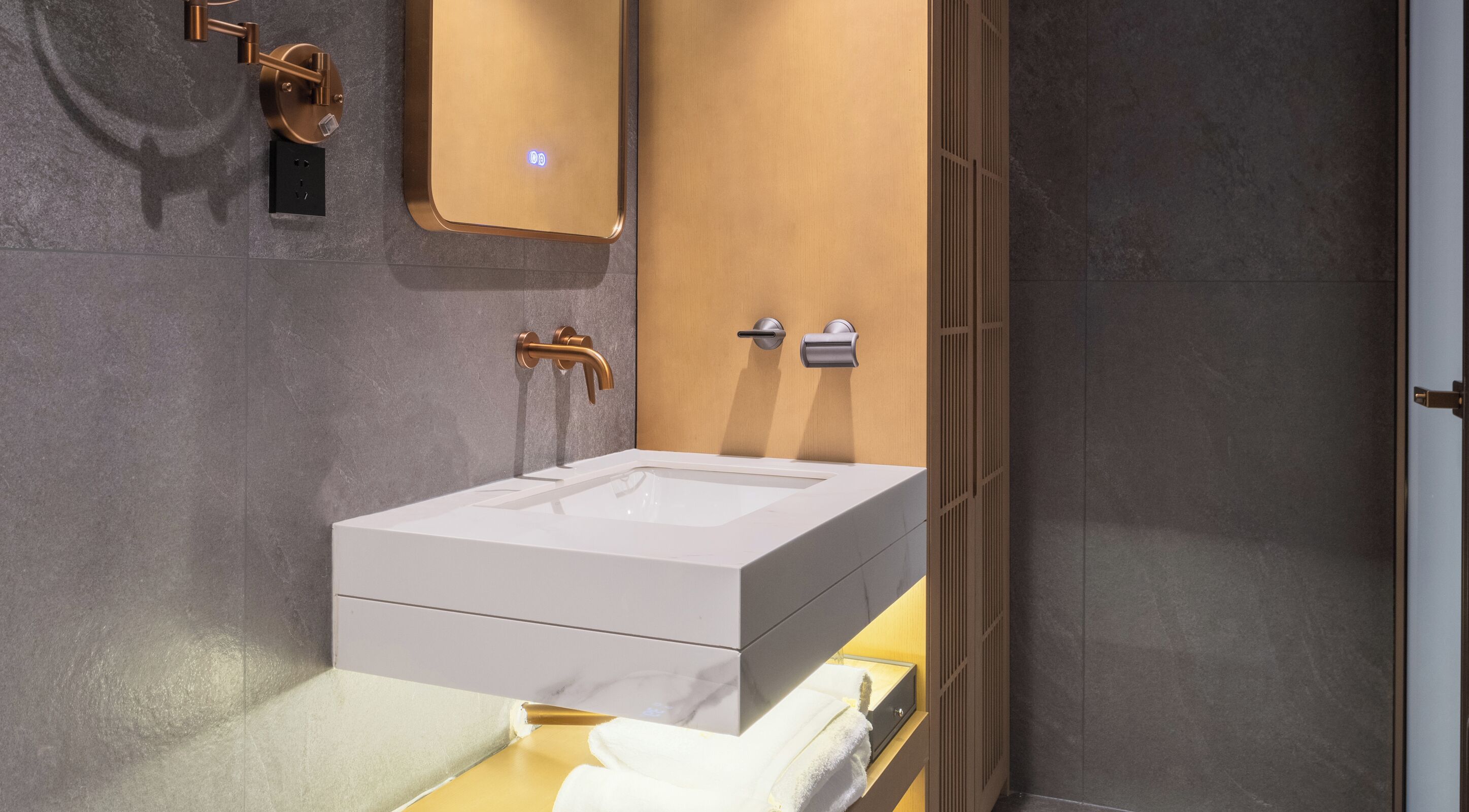 Ein modernes Badezimmer mit Waschbecken in Weiß, goldenen Armaturen und einem Holz-Waschtisch.