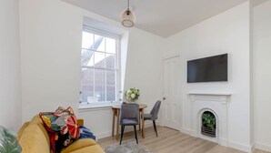 Una sala de estar con sofá, chimenea, televisor montado en la pared y un comedor con sillas y mesa.