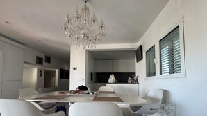 A modern dining area with a chandelier, white furniture, and a kitchen in the background. - Ibiza Serenity Estate (Can fornet)