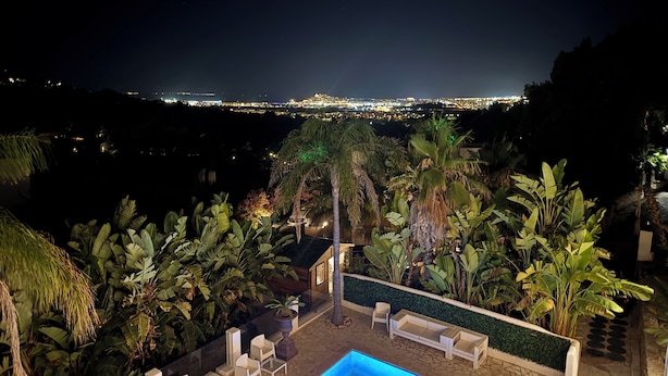 A pool area with chairs and a table, surrounded by tropical plants, overlooking a cityscape at night. - Ibiza Serenity Estate (Can fornet)