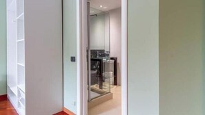 Ein Flur, der zu einem Badezimmer mit Glastrennwand, Waschbecken und Spiegel führt.