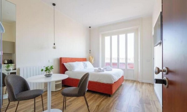 Ein Hotelzimmer mit einem Bett, einem kleinen Tisch, zwei Stühlen, einem Blumentopf und einem Fenster.